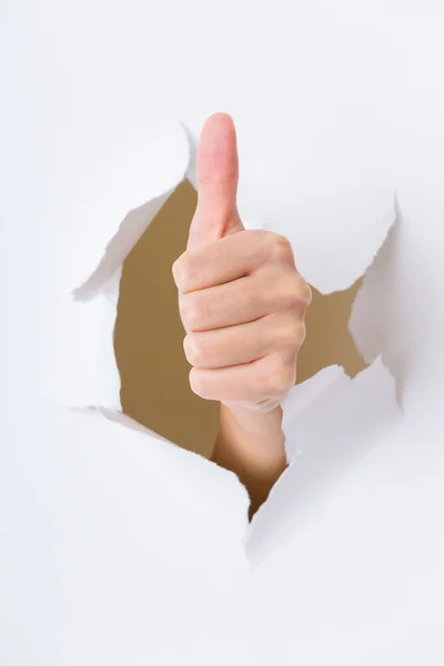 Hand through the hole in paper with woman thumb up — Stock Photo, Image
