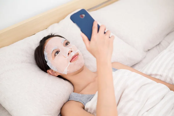 Vrouw met gezichts masker met behulp van mobiele telefoon — Stockfoto