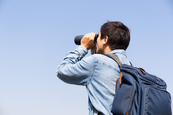 Man looking though the binocular against blue sky