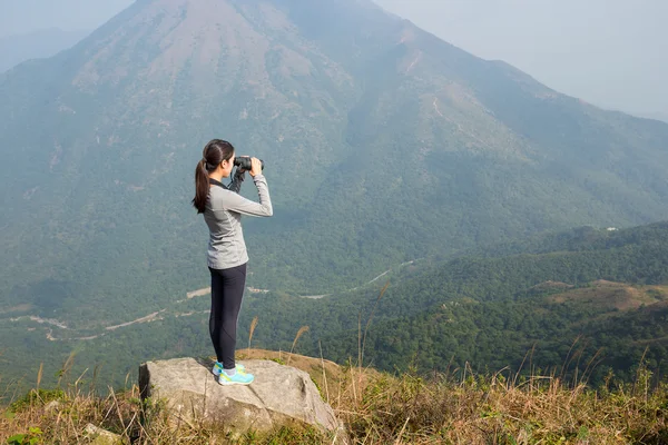 Woman looking though binoculars at mountain — Stock Photo, Image