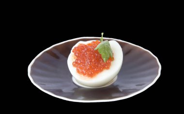 İştah açıcı kırmızı havyar yarım yumurta ve çay tabağı siyah üzerine izole edilmiş.