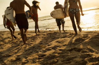 Sörf tahtasıyla okyanusa koşan arkadaşların grup fotoğrafı.