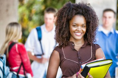 Üniversite kampüsünde, arka planda sınıf arkadaşlarıyla gülümseyen Afrikalı Amerikalı kız öğrenci portresi.