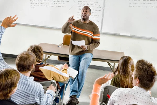 教室で手を挙げている大学生を指差す教授 — ストック写真