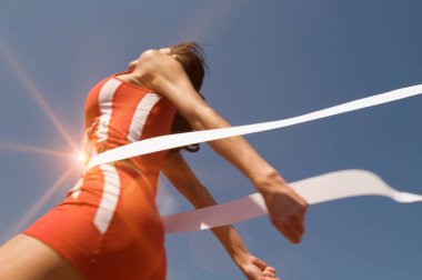 Açık mavi gökyüzüne karşı bitiş çizgisini geçen genç bayan sporcunun düşük açılı görüntüsü
