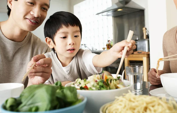 年幼的父母看着儿子在饭桌上用筷子 — 图库照片