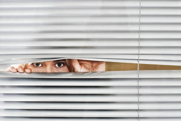 Young woman looking through Venetian blinds