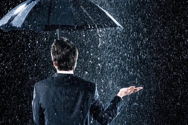 大雨倾盆时一个商人在伞下保持干燥的后视镜 免版税图库图片