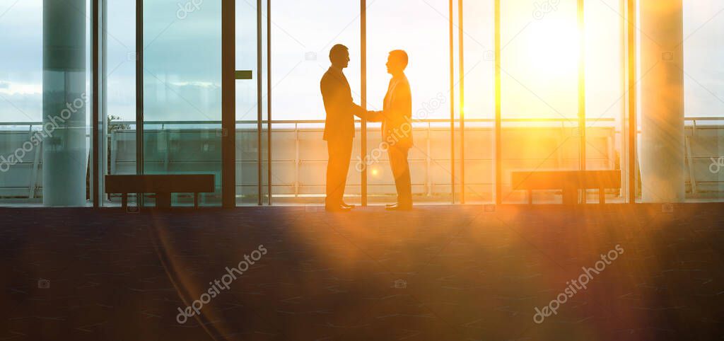 Two silhouette businessmen shaking hands in the airport lobby