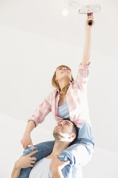 Woman on man's shoulders painting ceiling with paint roller