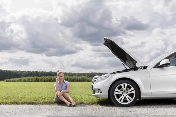 Businesswoman sitting by broken down car — Stock Photo, Image