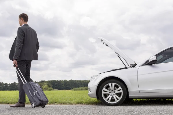 Businessman with suitcase leaving broken down car — Stock Photo, Image