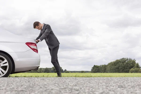 Businessman pushing broken down car — Stock Photo, Image