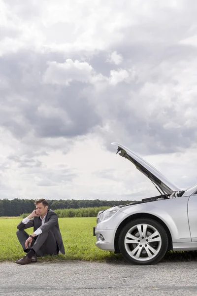 Young businessman sitting by broken down car — Stock Photo, Image