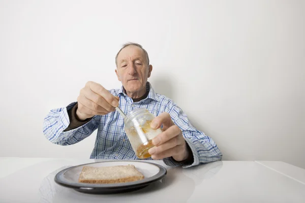Senior bereitet Scheibe Brot und Marmelade zu — Stockfoto