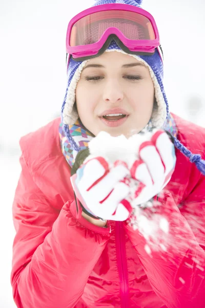 Woman wearing winter coat blowing snow outdoors — Stock Photo, Image