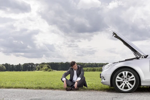 Young businessman sitting by broken down car — Stock Photo, Image