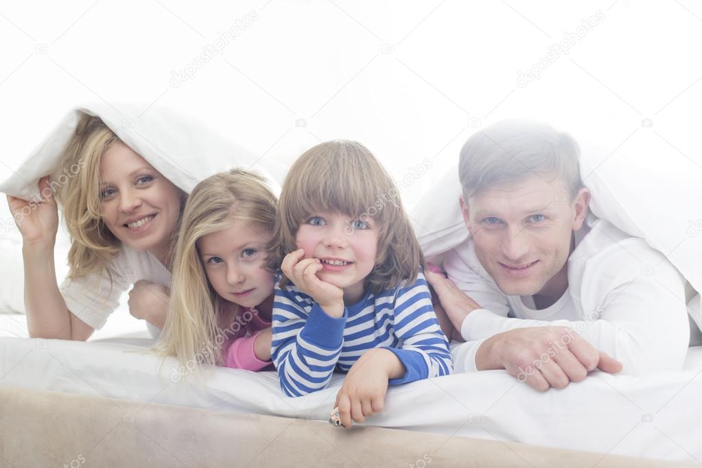 Parents and children lying under bed cover
