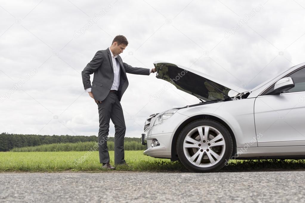 Businessman examining car engine