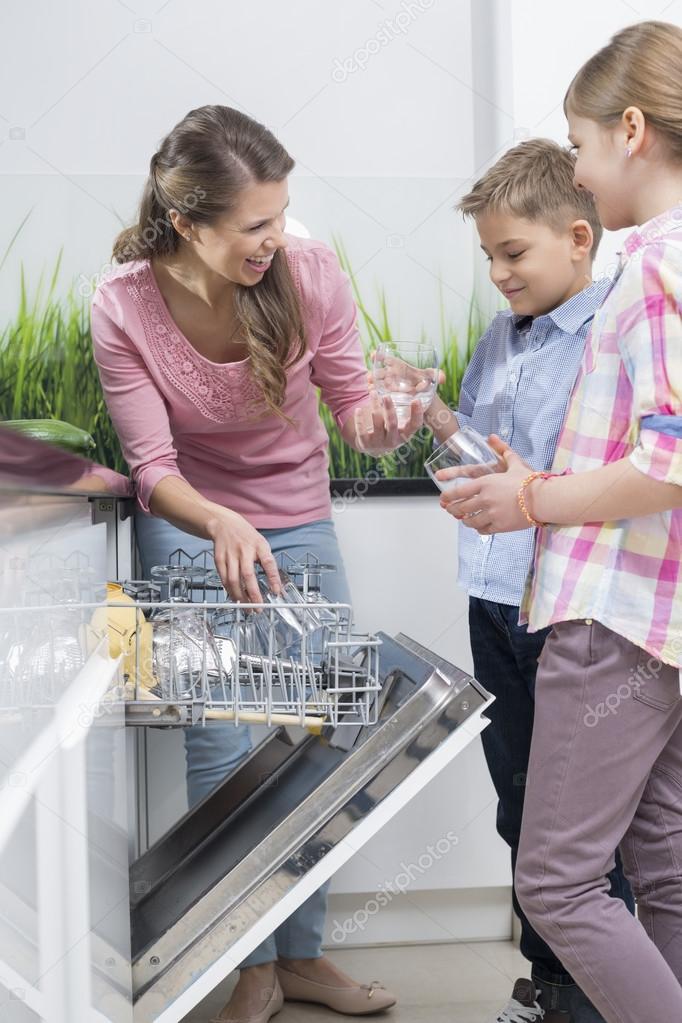 Mother and children placing glasses in dishwasher