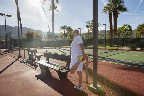 Jugador de tenis estirando la pierna en la cancha —  Fotos de Stock