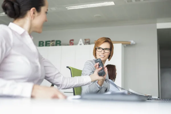 Businesswoman handing telephone to colleague