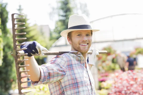 Glimlachend tuinman uitvoering hark op schouders — Stockfoto