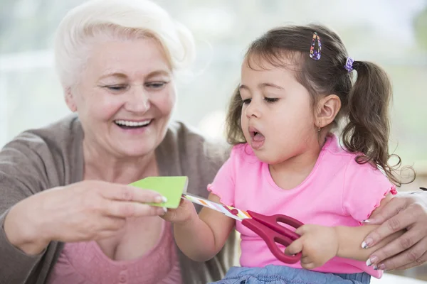Vrouw met kleindochter snijden papier — Stockfoto