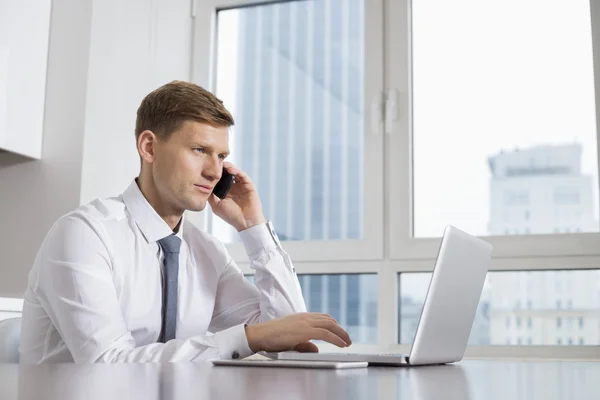 Businessman on call while using laptop — Stock Photo, Image