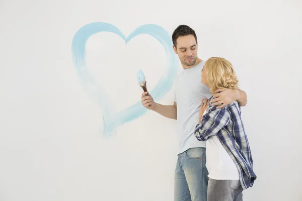 Couple with painted heart on wall — Stock Photo, Image
