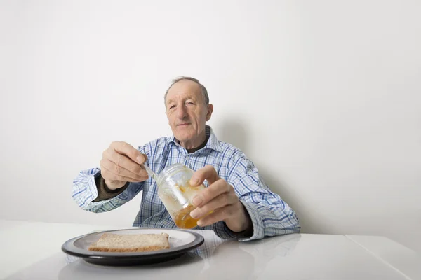 Äldre man förbereda skiva bröd och marmelad — Stockfoto