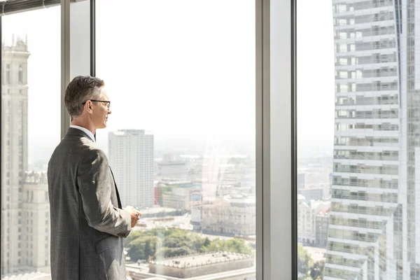 Businessman looking through office window — Stock Photo, Image