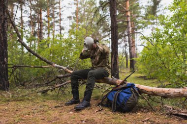Gaz maskeli silahlı bir asker ormanda yürüyor ve düşmanı takip ediyor.
