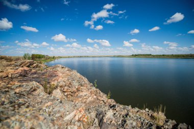 Beyaz bulutlar mavi gölün üzerinde yavaşça süzülür.