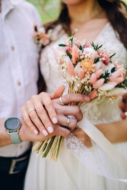 Gelin ve damat çok güzel bir düğün buketi tutuyor.