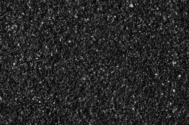 Kaba siyah zımpara kağıdının son derece büyütülmüş görüntüsü, pürüzsüz veya parlatıcı yüzeylerde kullanılan kumlu aşındırıcı dokusunu gösteriyor.