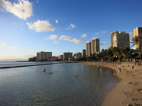 Menschen spielen in der Abenddämmerung im Wasser und am Strand in Waikiki — Stockfoto