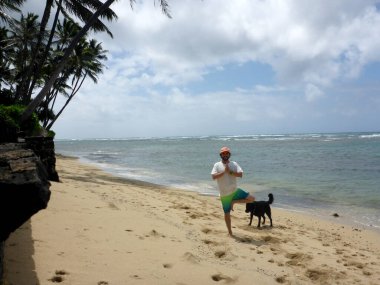 Adam, Hawaii 'de sahilde bir köpeğin yanında elleri dua ederken Yoga Pozu yapıyor..