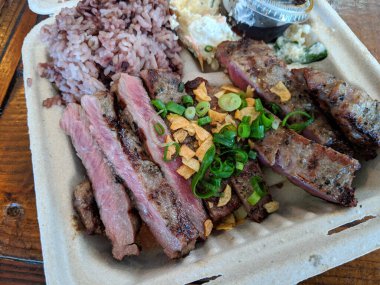 Plastik bir kabın içinde ju soslu, fasulye pilavlı ve patates salatalı orta pişmiş pirzola..