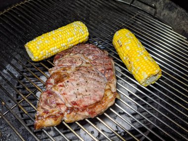 Steak and Two pieces of Corn cooking on a grill.