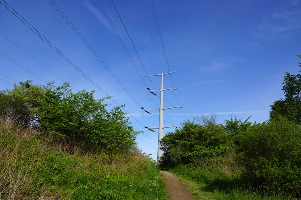 Chemin de terre menant à la colline avec poteau électrique en métal dans le distan — Photo