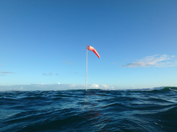 Flag pole with wind sock rises above the wavy waters of Waikiki