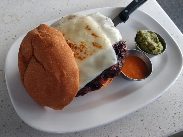 Large Swiss Cheese Hamburger with guacamole, and hot sauce sides — Stock Photo, Image