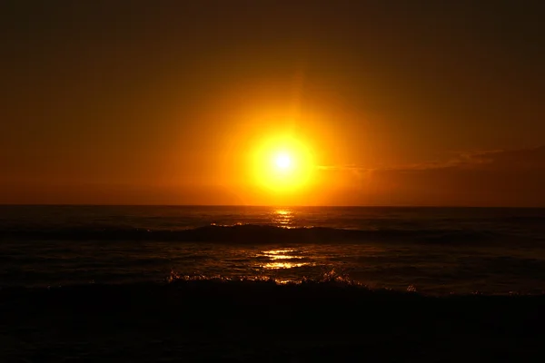 Salida del sol sobre el océano con olas rompiendo a lo largo de la orilla — Foto de Stock