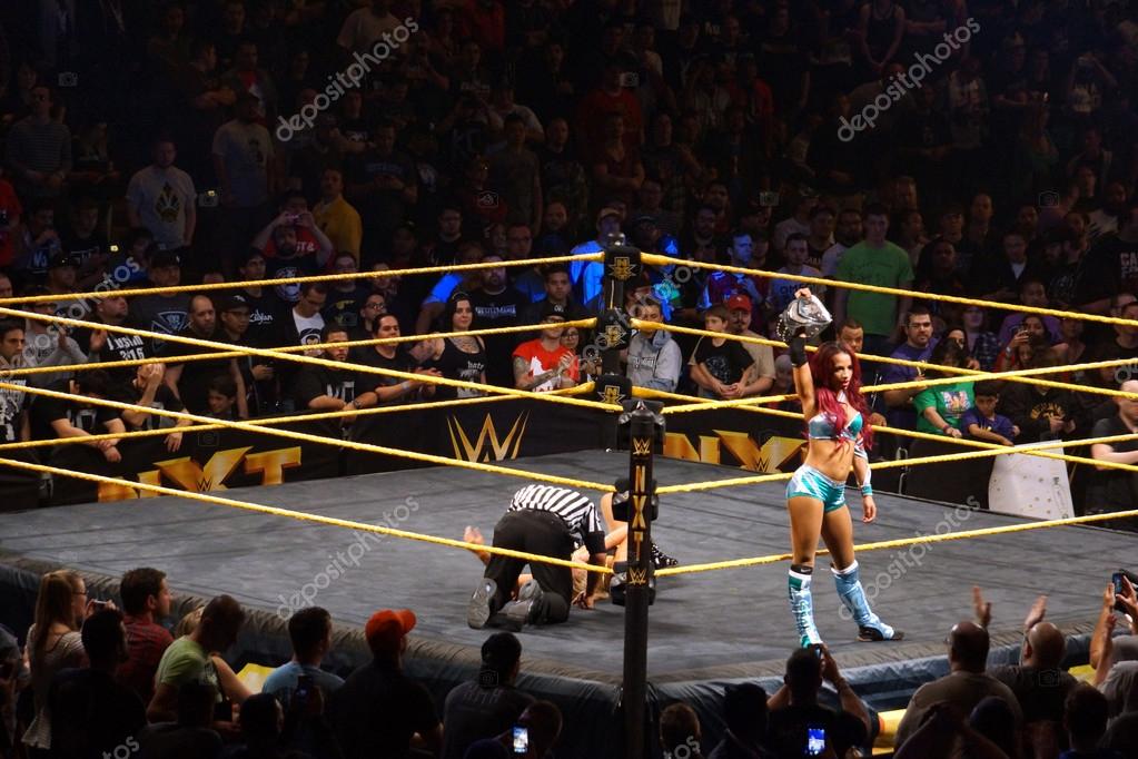 SAN JOSE - MARCH 27: NXT Female wrestlers Sasha Banks holds Womens Championship title overhead on ring apron as wrestle Charlotte Flair lays on the ground being check on by ref in ring after divas championship match at the San Jose Event Center in Sa