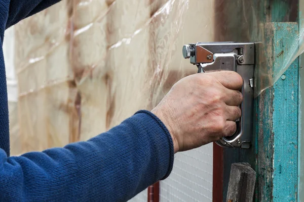 Builder fixes polyethylene film with staple gun — Stock Photo, Image