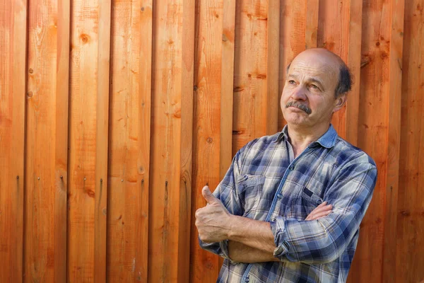 Homem idoso olhando para longe sonhadoramente em um fundo de madeira — Fotografia de Stock