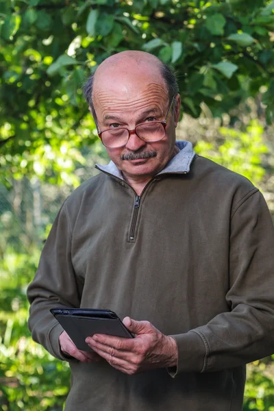 Äldre man med en flintskalle, mustasch och glasögon lära sig att hantera tablet. — Stockfoto