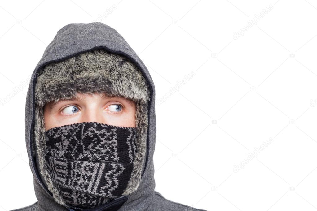 Young man in hat, scarf and hood hiding from the cold weather in