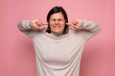 Gürültüden kaçınmak için kulaklarını tıkayan sinirli genç bir kadın.